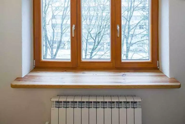Light oak timber window frame with triple casement, snowy urban exterior view, closed position, wood sill and radiator inside — Cristal Windows, Doors & Conservatories