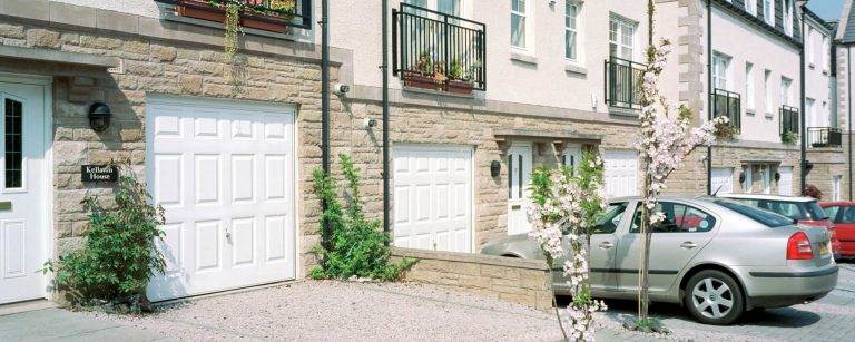 Row of modern homes with white panelled garage doors and stone facades – Cristal Windows, Doors & Conservatories