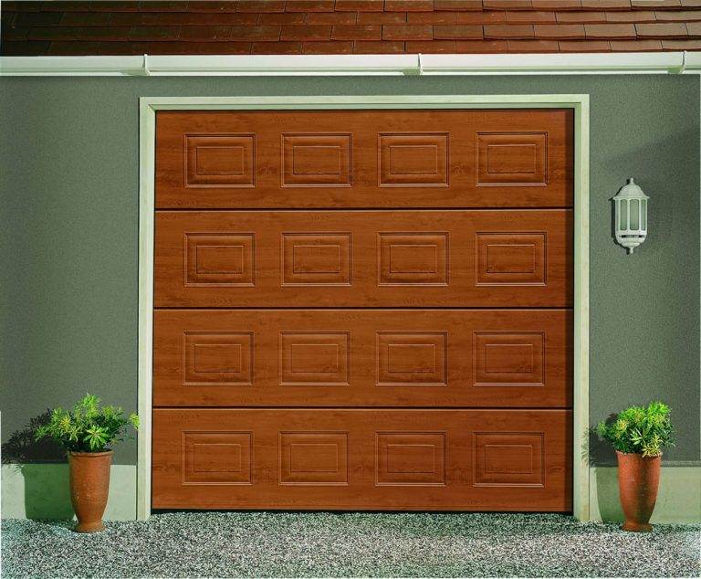 Golden oak sectional garage door with rectangular panel detailing, framed by grey exterior walls and decorative potted plants – Cristal Windows, Doors & Conservatories
