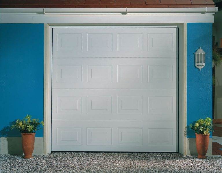 White sectional garage door with rectangular panel design installed on a blue-painted home exterior – Cristal Windows, Doors & Conservatories