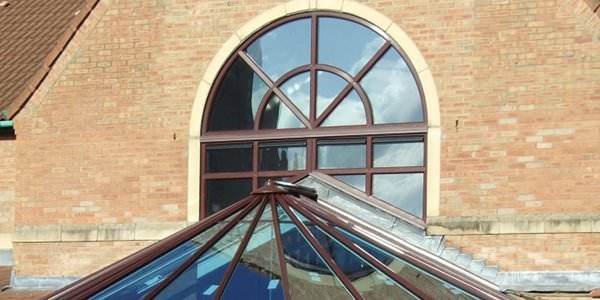 Arched bespoke timber window with decorative glazing bars set in brick wall, reflecting sky and clouds – Cristal Windows, Doors & Conservatories