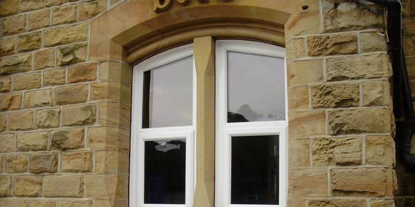 White arched bespoke casement window set in stone wall with decorative sandstone surround – Cristal Windows, Doors & Conservatories
