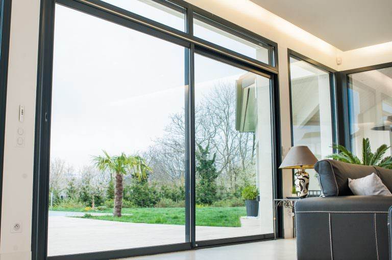 Interior view of black-framed aluminium patio doors opening to garden with palm trees – Cristal Windows, Doors & Conservatories