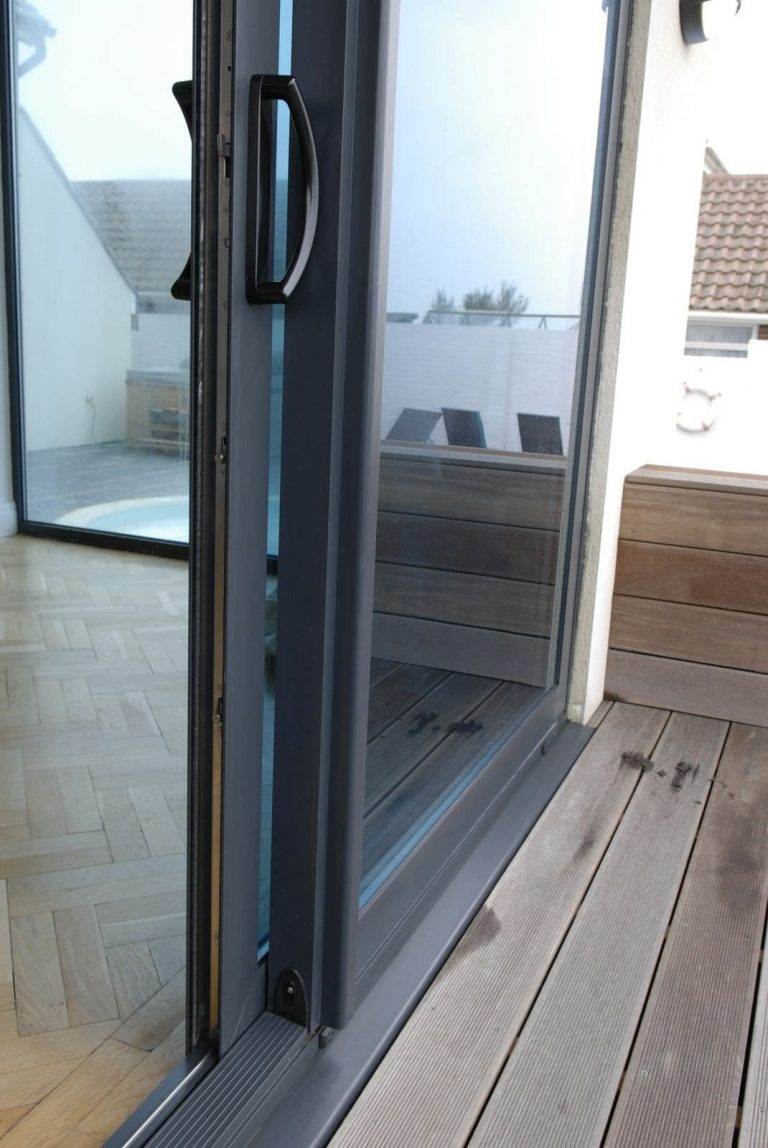 Close-up view of black-framed aluminium patio door with handle, opening to decked balcony – Cristal Windows, Doors & Conservatories