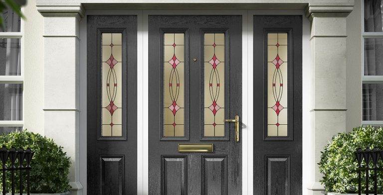 Black composite front door with decorative stained glass panels and gold hardware, framed by matching side lights – Cristal Windows, Doors & Conservatories