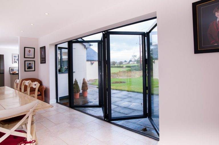Interior view of open aluminium bi-fold doors in black frame leading to garden patio – Cristal Windows, Doors & Conservatories