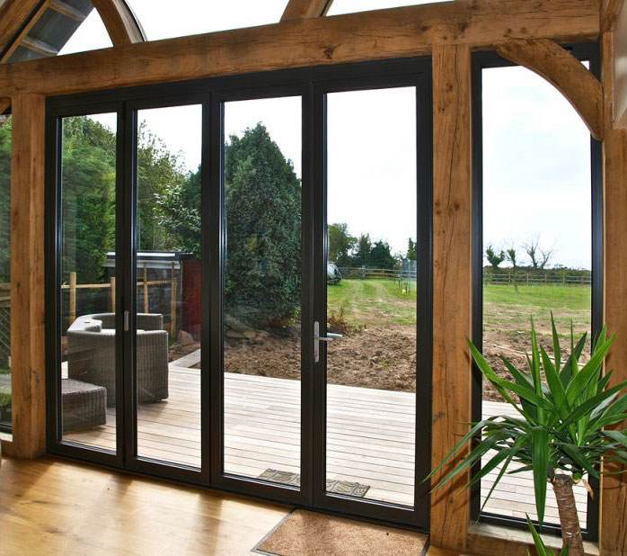 Interior view of closed aluminium bi-fold doors in black frame overlooking garden and deck – Cristal Windows, Doors & Conservatories