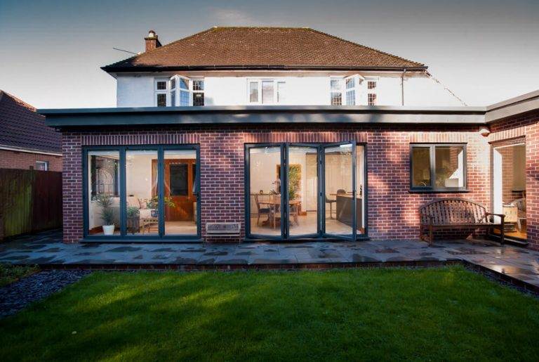 Exterior view of modern home with aluminium bi-fold doors in black frame opening to garden – Cristal Windows, Doors & Conservatories