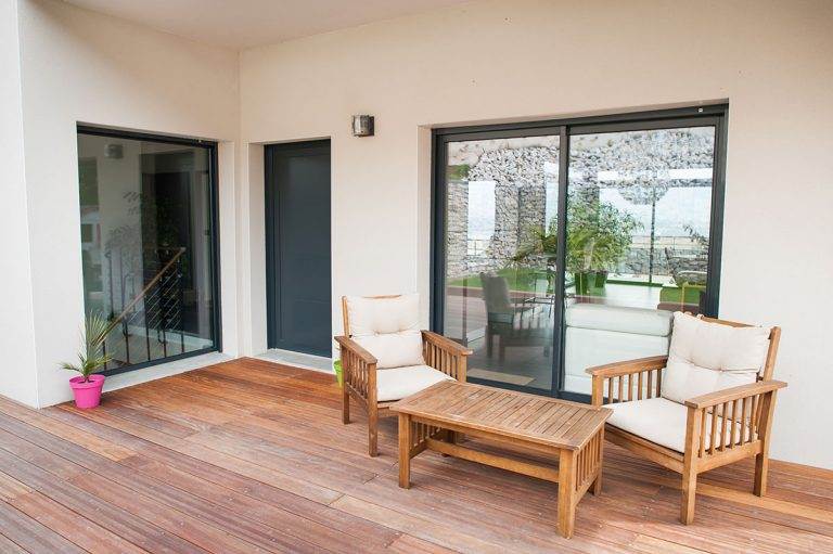 Exterior view of aluminium patio doors in dark frame opening onto wooden deck with outdoor seating – Cristal Windows, Doors & Conservatories
