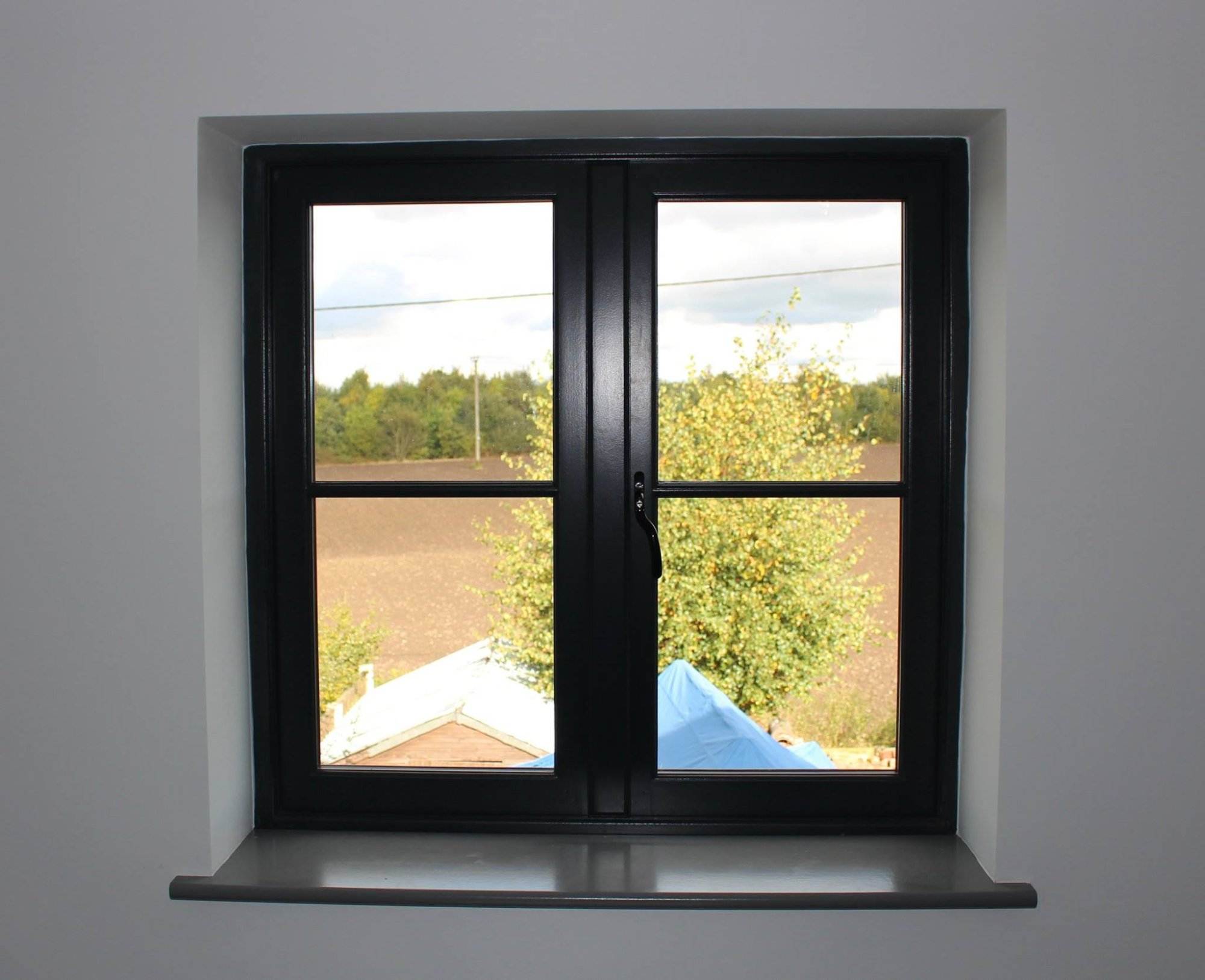 Black timber casement window with a rural view, closed position, white interior wall — Cristal Windows, Doors & Conservatories