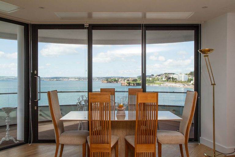 Dining room with black-framed aluminium patio doors opening to balcony with panoramic sea view – Cristal Windows, Doors & Conservatories