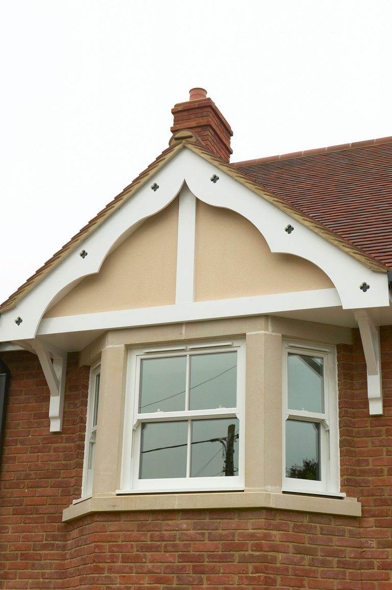 White uPVC sliding sash bay window on a red brick gable with decorative timber detailing – Cristal Windows, Doors & Conservatories
