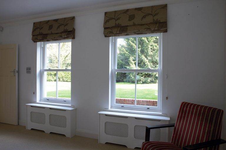 Interior view of two white uPVC sliding sash windows with Roman blinds in a bright living space – Cristal Windows, Doors & Conservatories