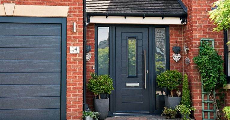 Modern dark grey composite front door with vertical glazed panel and matching side lights set in red brick home – Cristal Windows, Doors & Conservatories