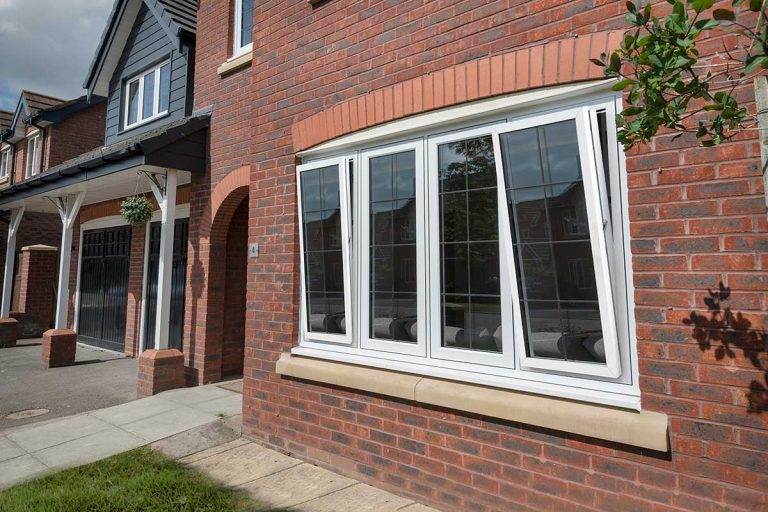 White uPVC tilt and turn window with grid-style glazing partially open on a modern red brick home – Cristal Windows, Doors & Conservatories