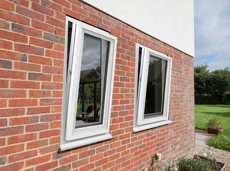 White uPVC tilt and turn windows partially open on a red brick exterior wall of a modern home – Cristal Windows, Doors & Conservatories