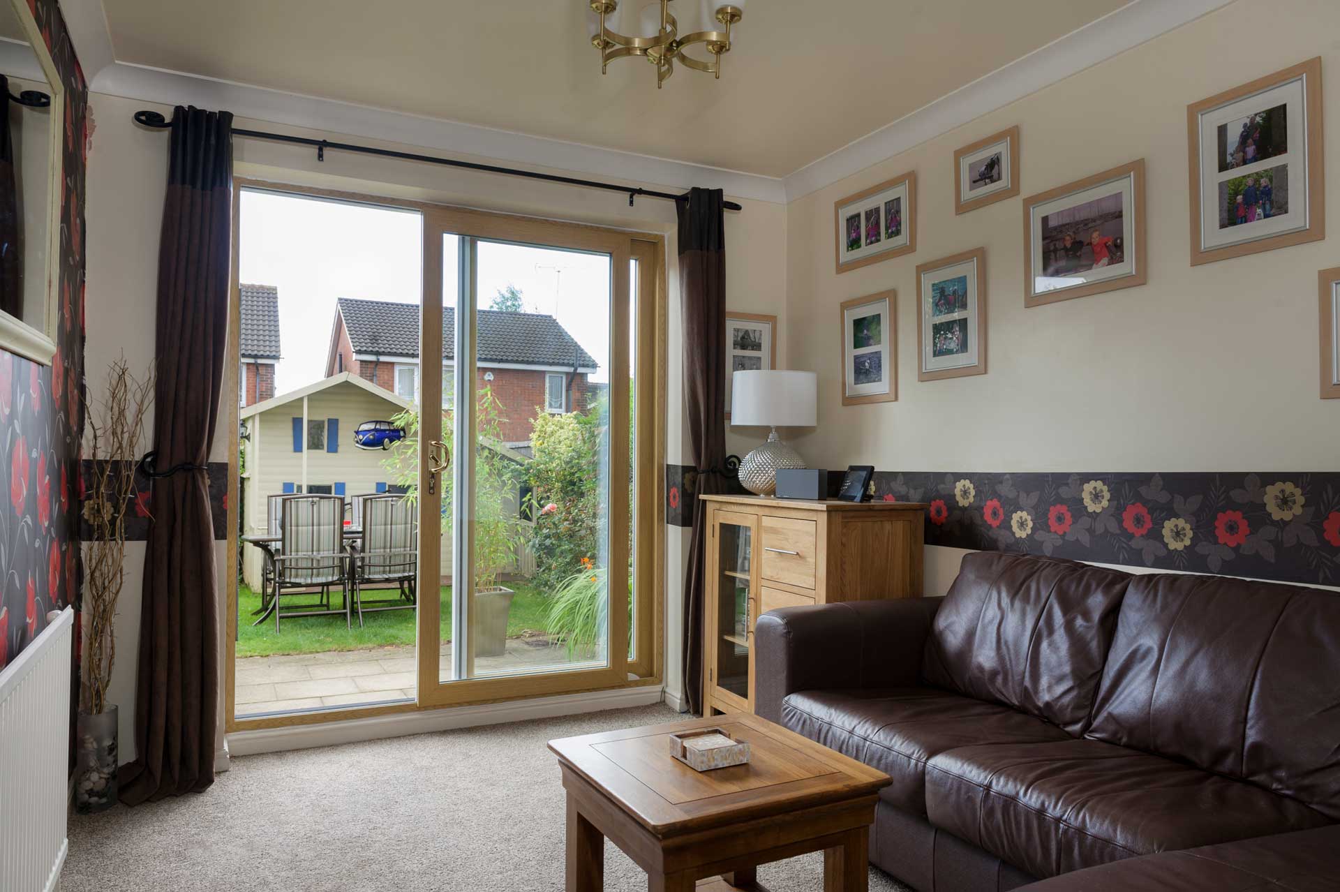 Cosy living room with brown leather sofa and wooden furniture, featuring uPVC patio sliding doors opening to a garden – Cristal Windows, Doors & Conservatories