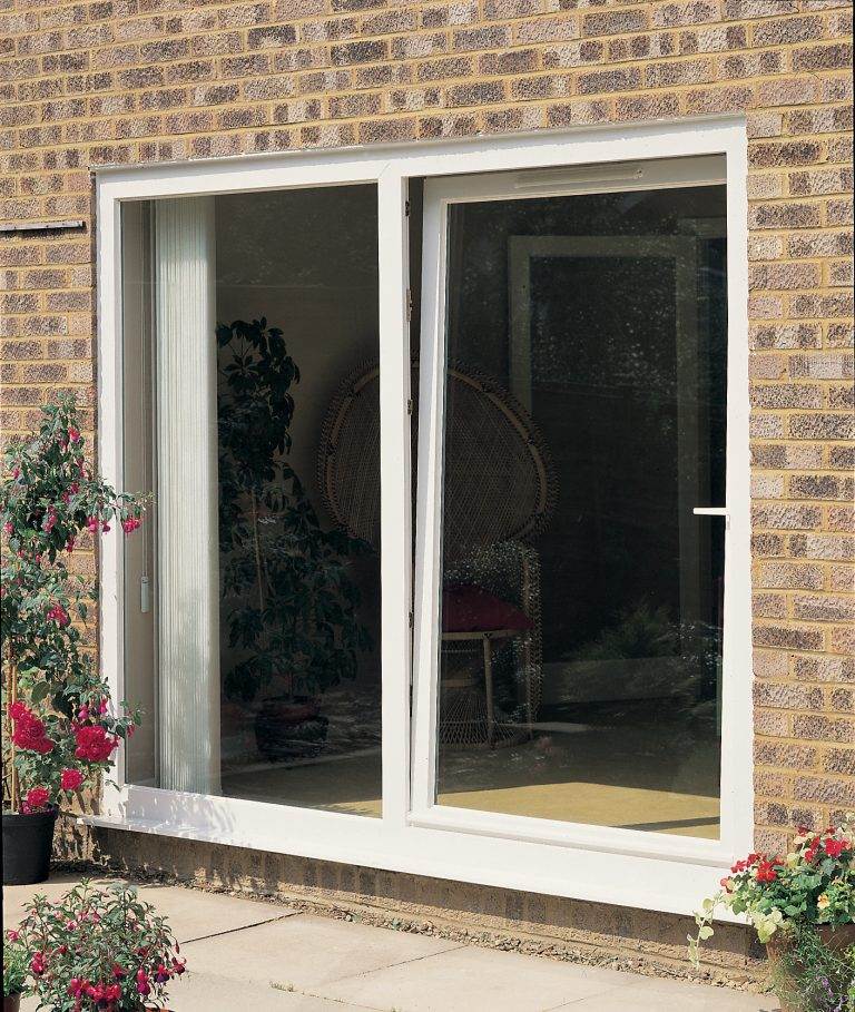 White uPVC tilt and turn window installed on a light brick home, partially open to a room with wicker furniture – Cristal Windows, Doors & Conservatories