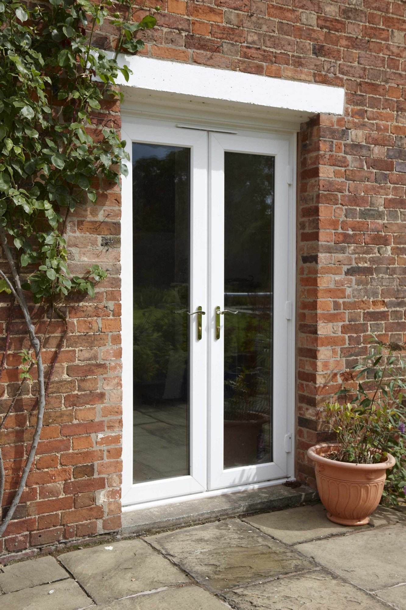 White uPVC French doors with glass panels and gold handles fitted into a red brick exterior – Cristal Windows, Doors & Conservatories