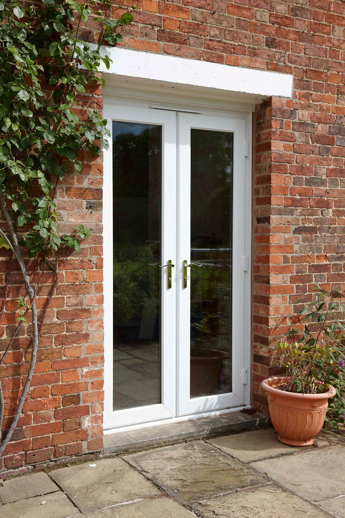 White uPVC French doors with glass panels and gold handles fitted into a red brick exterior – Cristal Windows, Doors & Conservatories