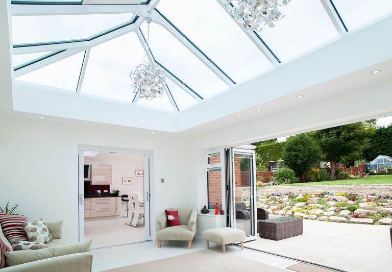 Bright living space with glass roof lantern and bi-fold doors opening to garden – Cristal Windows, Doors & Conservatories