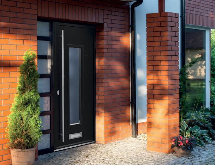 Modern black aluminium composite front door with long vertical glazed panel and chrome handle set in red brick wall – Cristal Windows, Doors & Conservatories