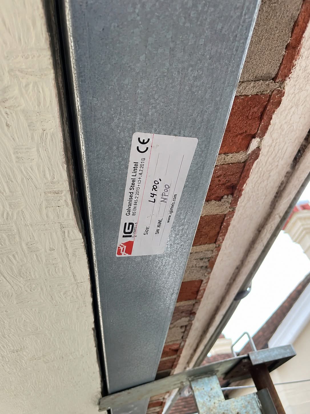 A new galvanised steel lintel installed above a window opening with its UKCA certification label visible