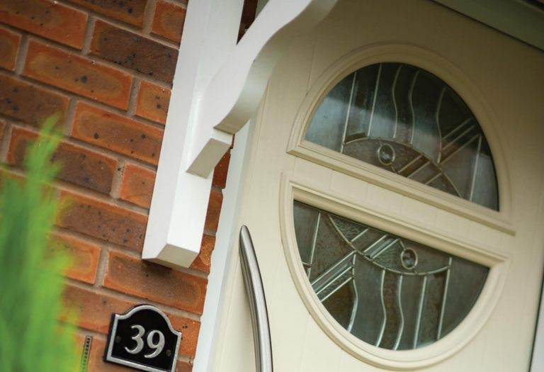Cream period front door with decorative circular glazed panels and chrome handle beside brick wall – Cristal Windows, Doors & Conservatories