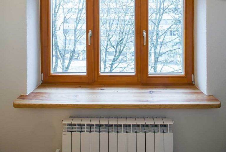 Light oak timber window frame with triple casement, snowy urban exterior view, closed position, wood sill and radiator inside — Cristal Windows, Doors & Conservatories