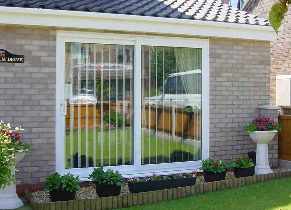 White uPVC patio sliding doors with vertical blinds, opening to a neatly landscaped garden – Cristal Windows, Doors & Conservatories