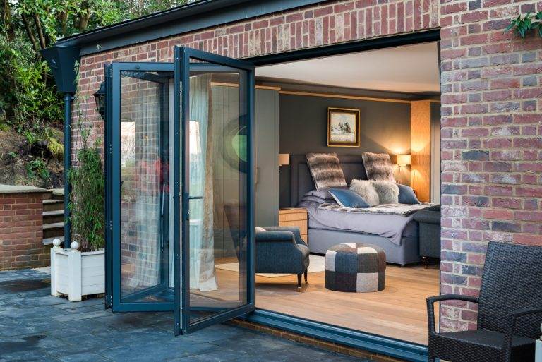 Open aluminium bi-fold doors in dark grey frame connecting bedroom to outdoor patio – Cristal Windows, Doors & Conservatories