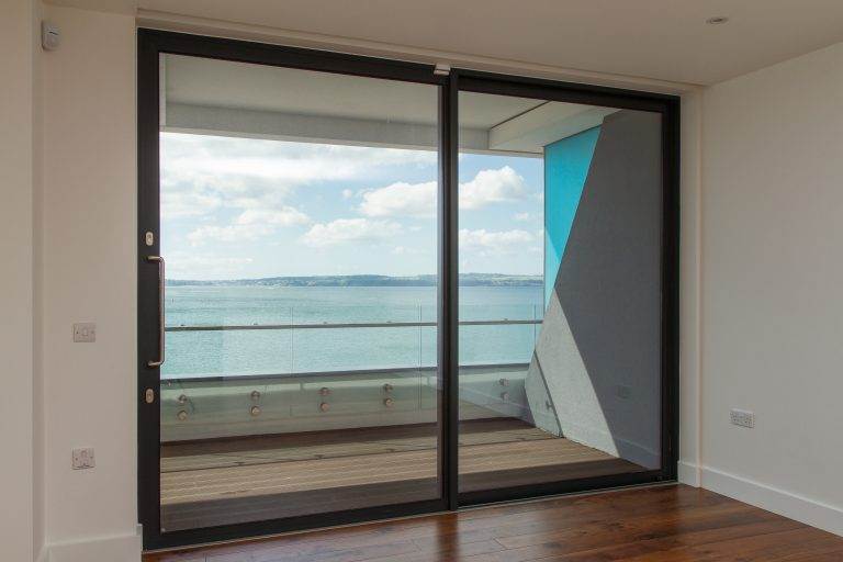 Interior view of black-framed aluminium patio doors opening to balcony with sea view – Cristal Windows, Doors & Conservatories