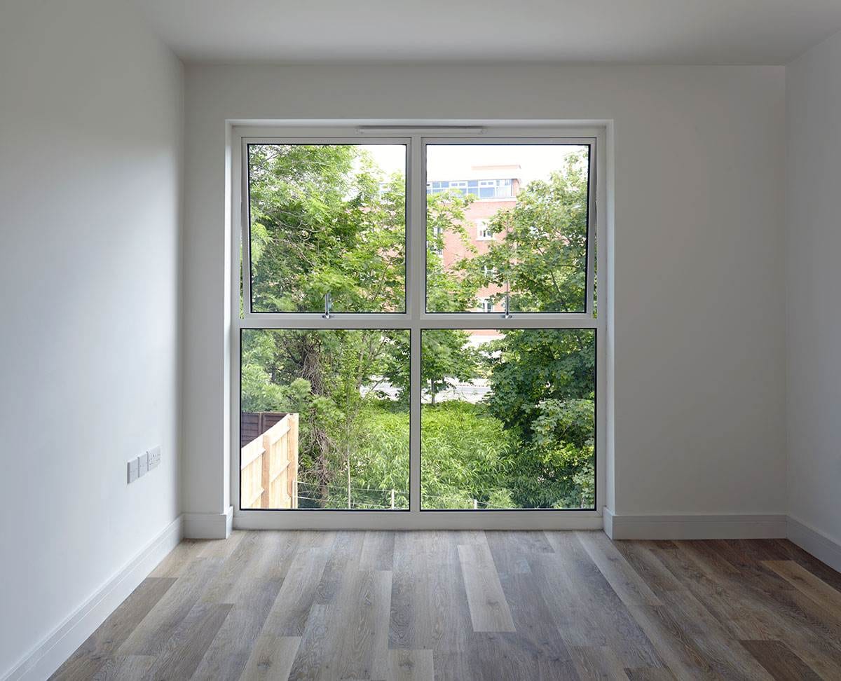 Modern white aluminium casement window with clear glazing, installed in a minimalist interior room with wood flooring and garden view — Cristal Windows, Doors & Conservatories.