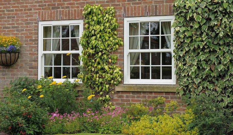 White uPVC sliding sash windows with Georgian bars on a brick cottage surrounded by flowers and ivy – Cristal Windows, Doors & Conservatories