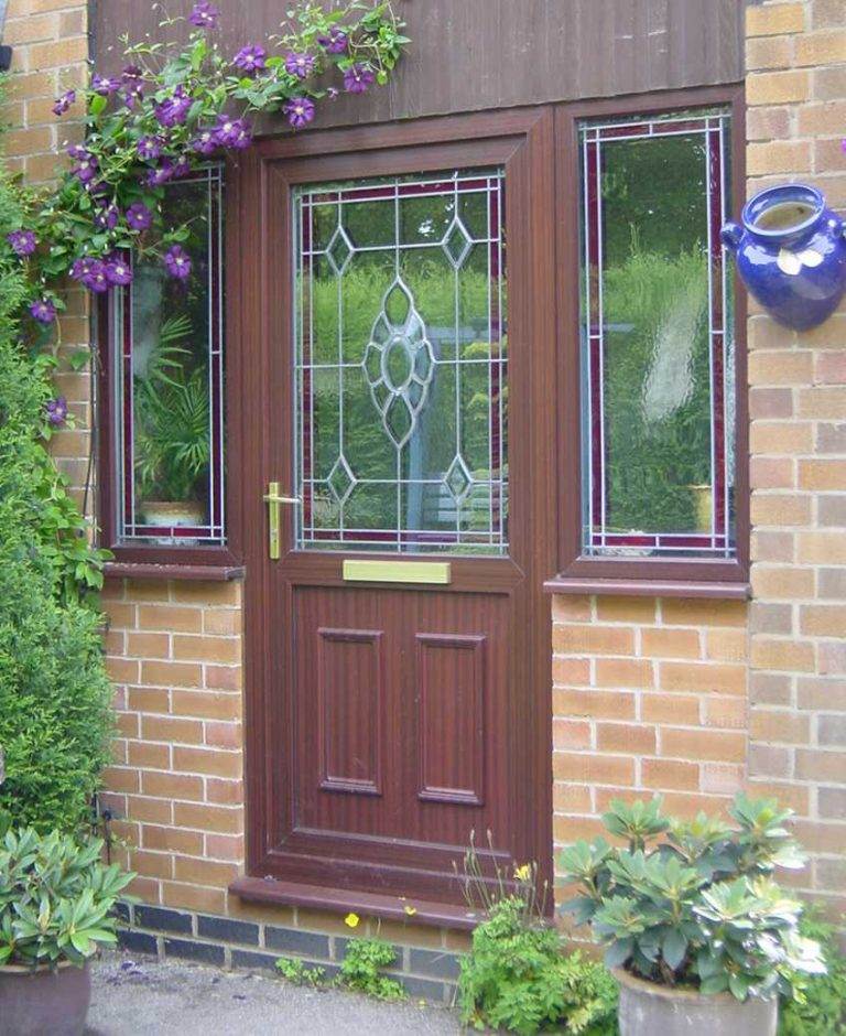 Wood-effect uPVC residential door with decorative leaded glass and gold handle, surrounded by matching side panels – Cristal Windows, Doors & Conservatories