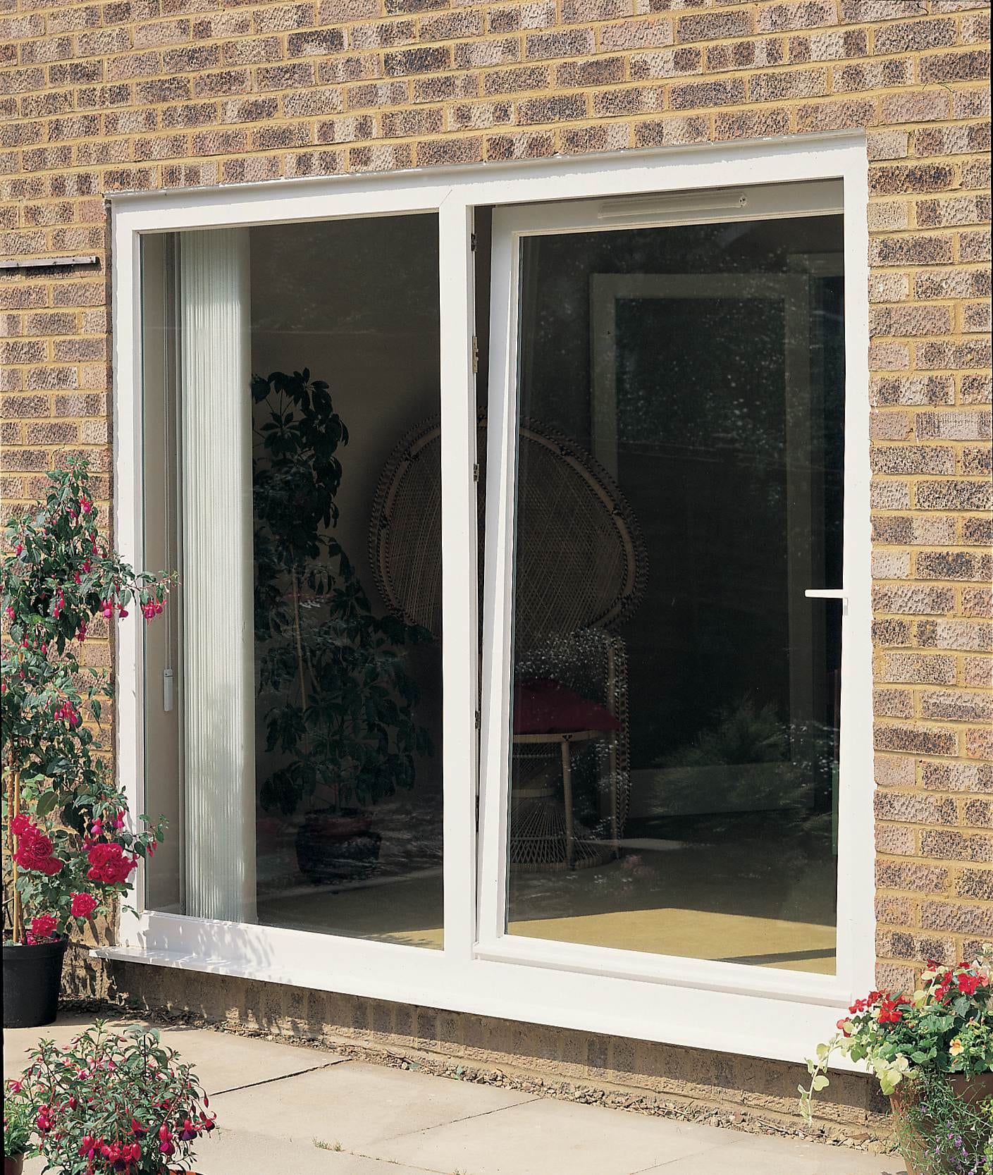 White uPVC tilt and turn window installed on a light brick home, partially open to a room with wicker furniture – Cristal Windows, Doors & Conservatories