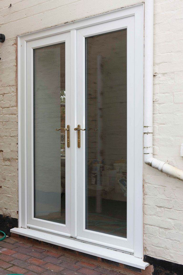 White uPVC French doors with gold handles fitted in a brick exterior – Cristal Windows, Doors & Conservatories