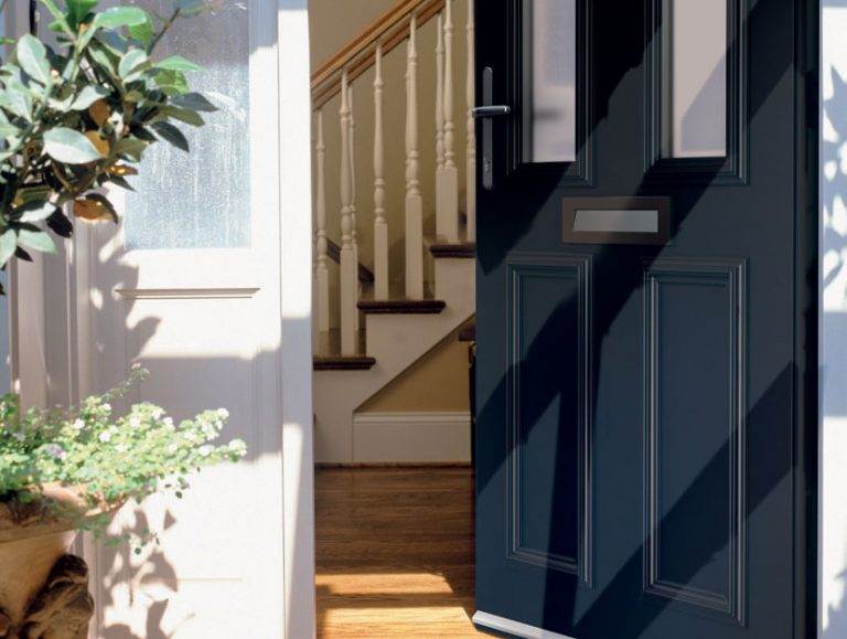 Partially open dark blue aluminium composite front door with vertical glazing and chrome handle leading into hallway – Cristal Windows, Doors & Conservatories